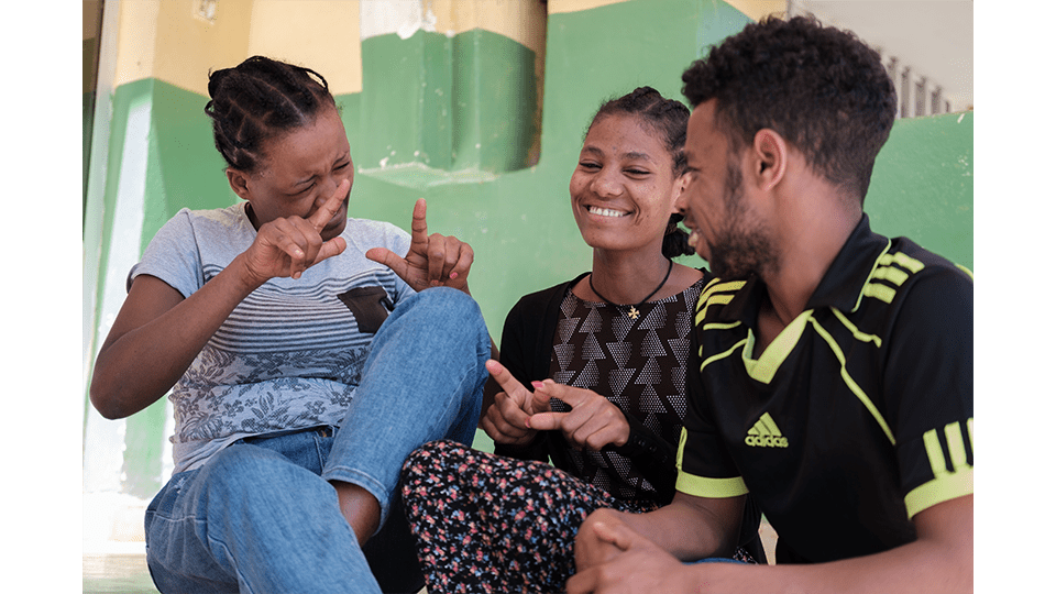 two young women to the right and a young man to the left using sign language to communicate