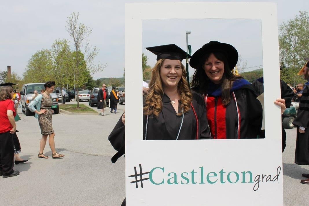 two women standing inside an instagram box, smiling. One is wearing a graduation hat