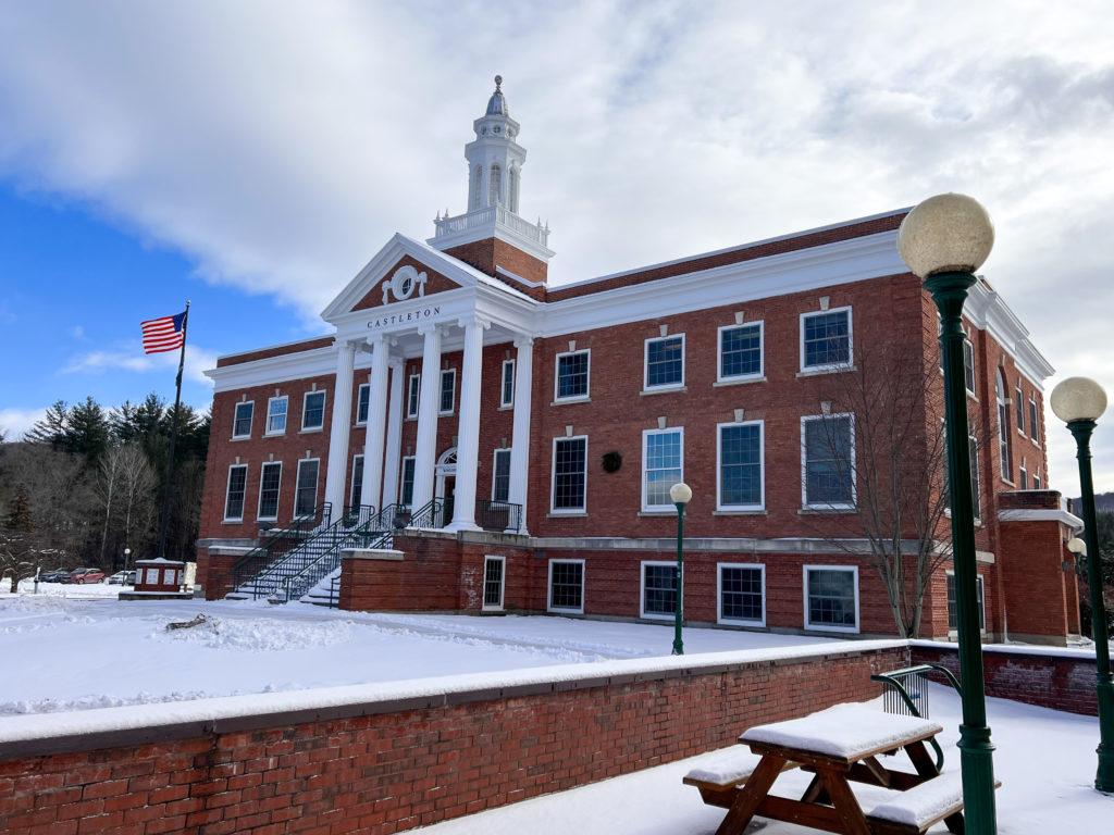 A photo of a large old brick building covered in snow. An American flag is flying next to the building