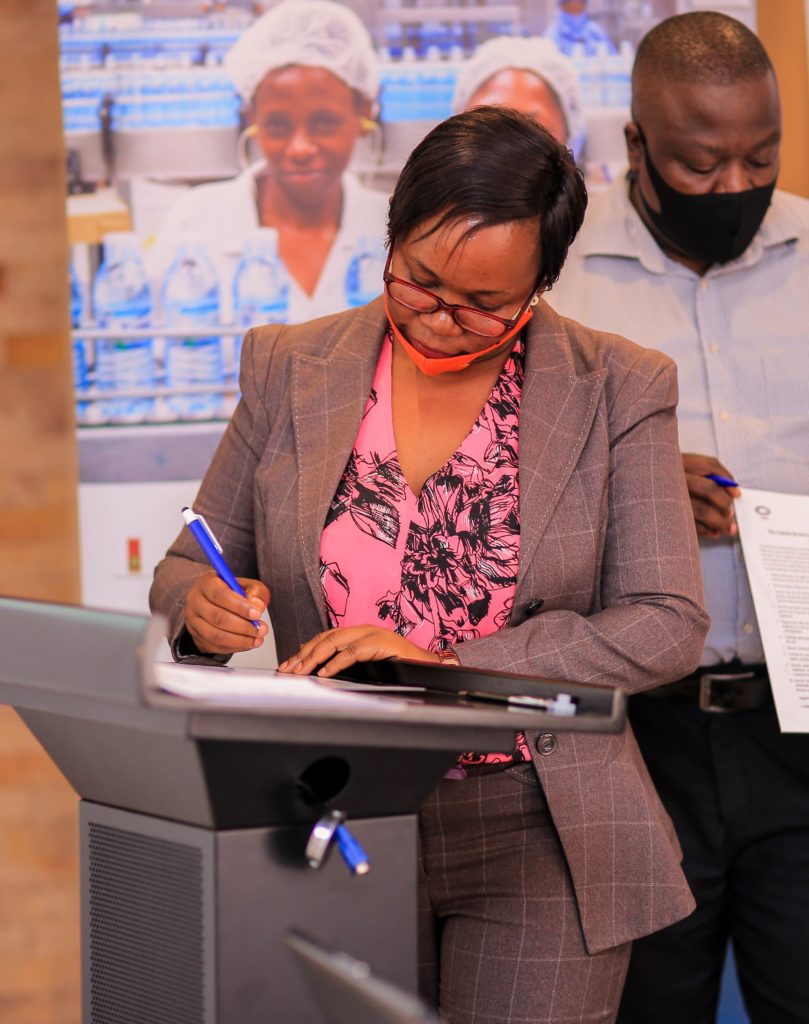 A woman in a grey blazer and pink pattered shirt signs the UBDN charter at a podium