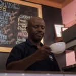 A man in a black shirt serves a cup of coffee