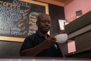 A man in a black shirt serves a cup of coffee